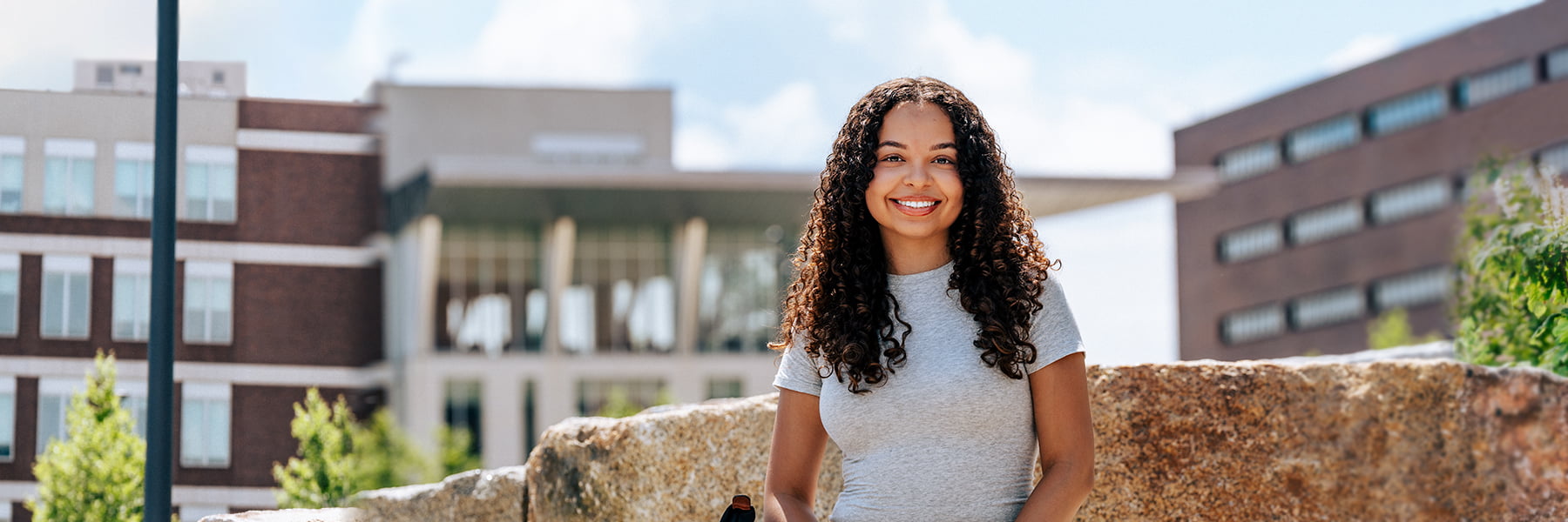 UMass Boston Female student sits on rock in Quad.