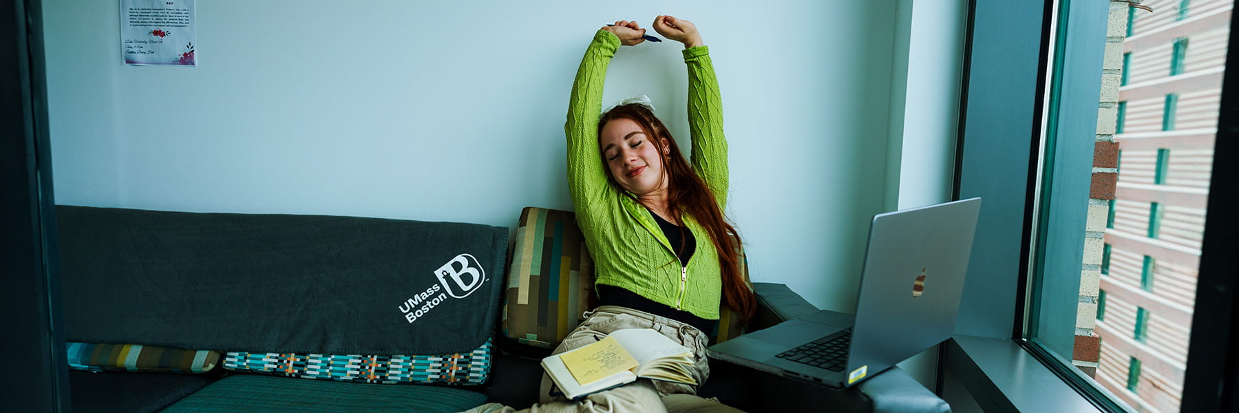 UMass Boston female student stretching as she studies on a couch