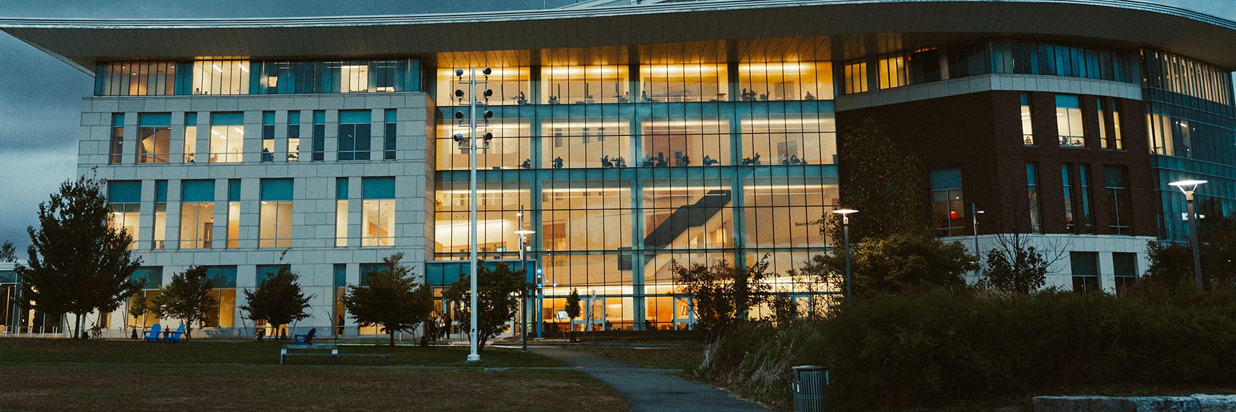 Floor to ceiling glass front of University Hall viewed from outside at night with lights glowing within.