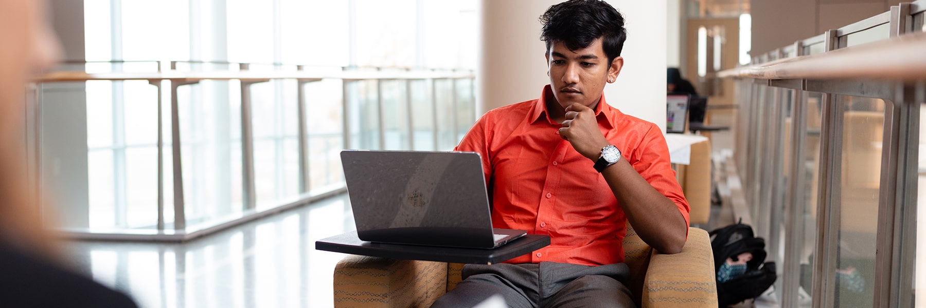Student works on laptop inddors by window inside University Hall.